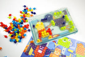 Conjunto Miniland Pegs com 150 peças de 15mm em cores vibrantes, um tabuleiro transparente e folhas de design com robôs. As peças estão espalhadas e algumas encaixadas no tabuleiro.