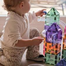 Criança pequena a brincar no chão, a colocar uma bola no topo de uma estrutura de blocos magnéticos Clever Clixx coloridos.