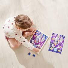 Criança deitada no chão a colorir um desenho de astronautas e alienígenas com lápis de cor, com o puzzle Hape Amigos no espaço ao lado.