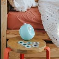 O projetor KidyStar repousa numa pequena mesa de madeira ao lado da cama, com os discos de projeção à frente.