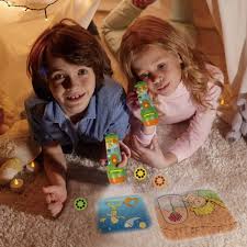 Duas crianças sorridentes, um rapaz e uma rapariga, deitadas em tapetes, a brincar com os projetores e as imagens projetadas no chão.