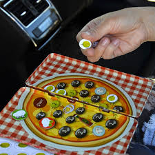 Mão a colocar um íman de azeitona na base do jogo "Pizza Race", que está aberto dentro de um carro, evidenciando o formato de viagem.