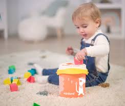 Bebé sentado no chão a brincar com o Miniland Cubo com formas de encaixe laranja, com várias peças espalhadas.