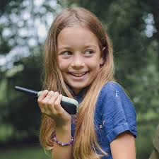 Uma menina sorridente segura um walkie talkie KidyWolf verde, olhando para o lado, num ambiente exterior.