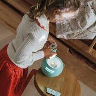 Criança inclinada a ajustar o projetor KidyStar, que está sobre um móvel, enquanto segura um telemóvel ou comando.