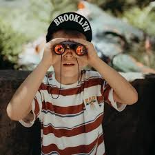 Menino curioso a usar os binóculos Kidywolf Verde para observar a natureza, mostrando a sua utilização em contexto de exploração.