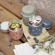 Dois termos Lassig de 350ml, um caramelo com massa e outro cinzento com iogurte e frutos vermelhos, sobre uma tábua de madeira rústica, com mirtilos e flores.