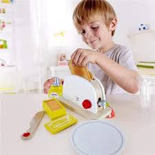 Criança a brincar com a Hape Torradeira, colocando uma fatia de pão no brinquedo de madeira, demonstrando a interação com o produto.