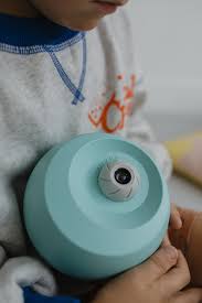 Detalhe das mãos de uma criança a segurar o projetor KidyStar esférico de cor verde-água.