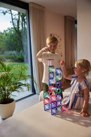 Duas crianças a brincar juntas numa sala iluminada, construindo uma torre vertical com os blocos magnéticos coloridos.