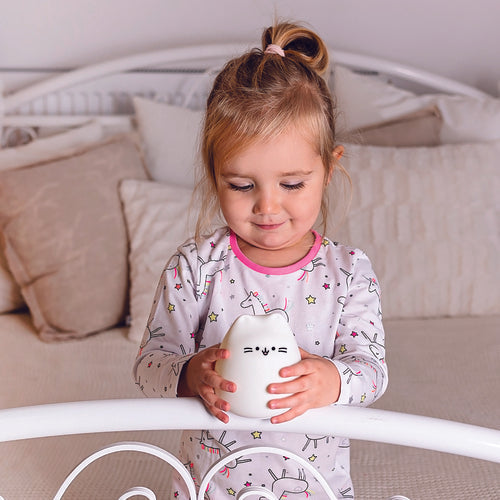 Criança pequena a segurar a luz de presença InnoGio Gatinho com as duas mãos, sorrindo num quarto com decoração clara.