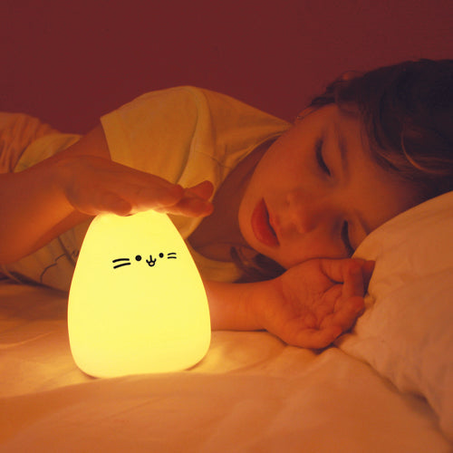 Criança a dormir pacificamente com a luz de presença InnoGio Gatinho ligada, emitindo um brilho amarelo quente na sua mão.