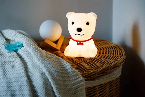 Criança pequena sentada na cama a segurar a luz de presença InnoGIO Cão, que está a emitir uma luz rosa suave.