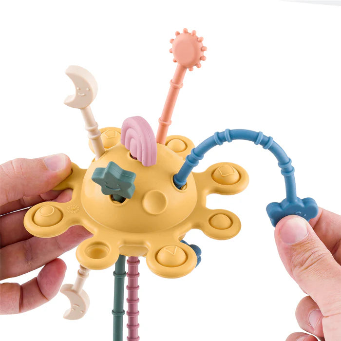 Mãos a interagir com o brinquedo sensorial, puxando uma das cordas azuis que se curva e faz um som.