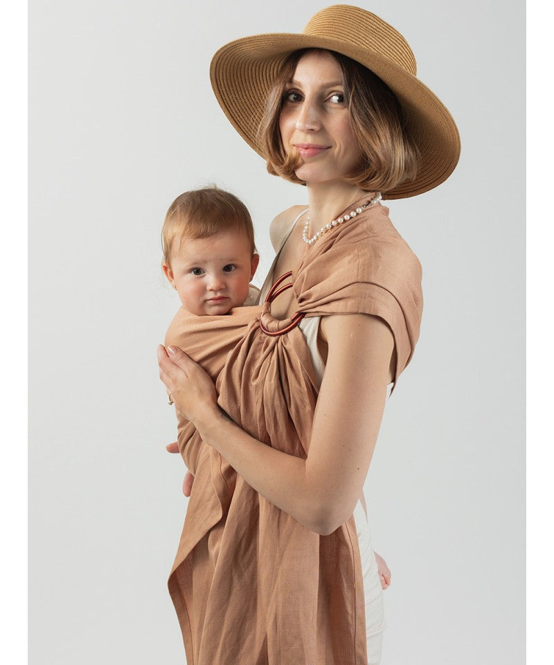 Mãe a usar Sling de Argolas Isara Caramel Bamboo Linen, vista lateral, mostrando a posição confortável do bebé.