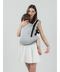 Mãe a carregar um bebé na frente, com a mochila Isara Preschooler PEARL GREY, em pose relaxada.