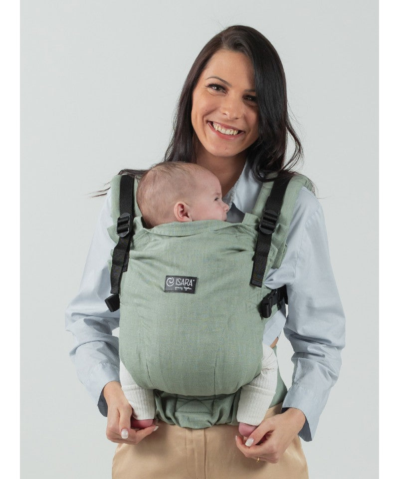 Mãe usando a mochila Isara The One Sage Green Linen, carregando uma criança de aproximadamente 2 anos.