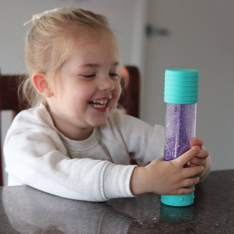 Criança sorridente a segurar a Garrafa da Calma DIY Jellystone com purpurinas roxas, focada na atividade sensorial.