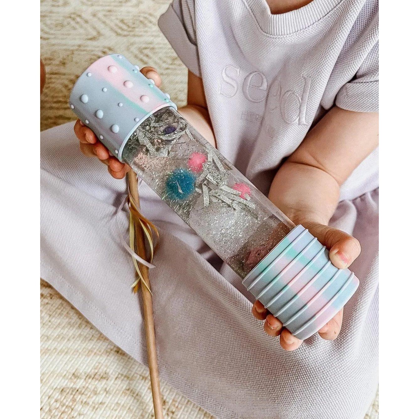 Criança a segurar a Garrafa da Calma DIY Jellystone com decorações coloridas (rosa e azul) para auto-regulação.