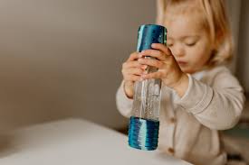 Criança pequena loira a segurar e observar atentamente a Garrafa da Calma DIY Galáxia Jellystone azul.
