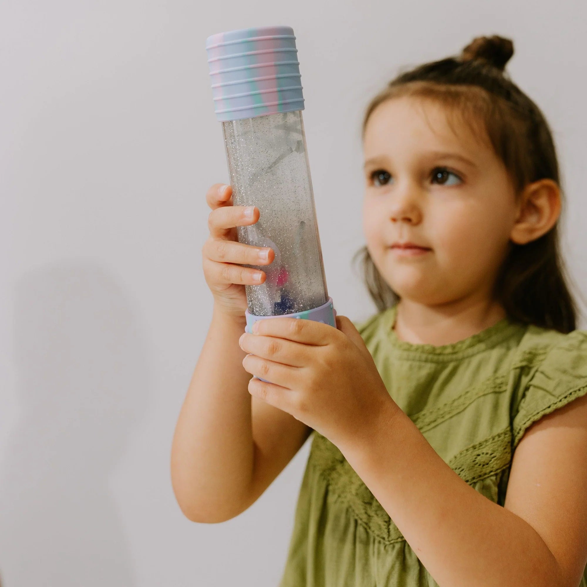 Menina a observar atentamente a Garrafa da Calma DIY Jellystone, que contém elementos sensoriais, promovendo a concentração.
