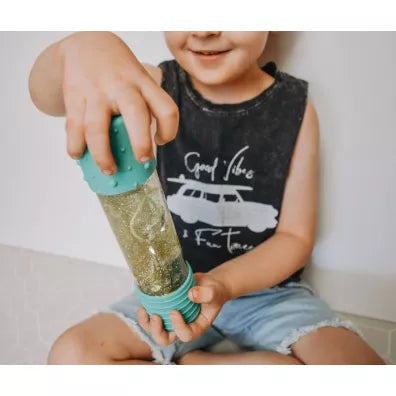 Mãos de criança seguram a Garrafa da Calma DIY Menta Jellystone, com brilhos verdes a flutuar.