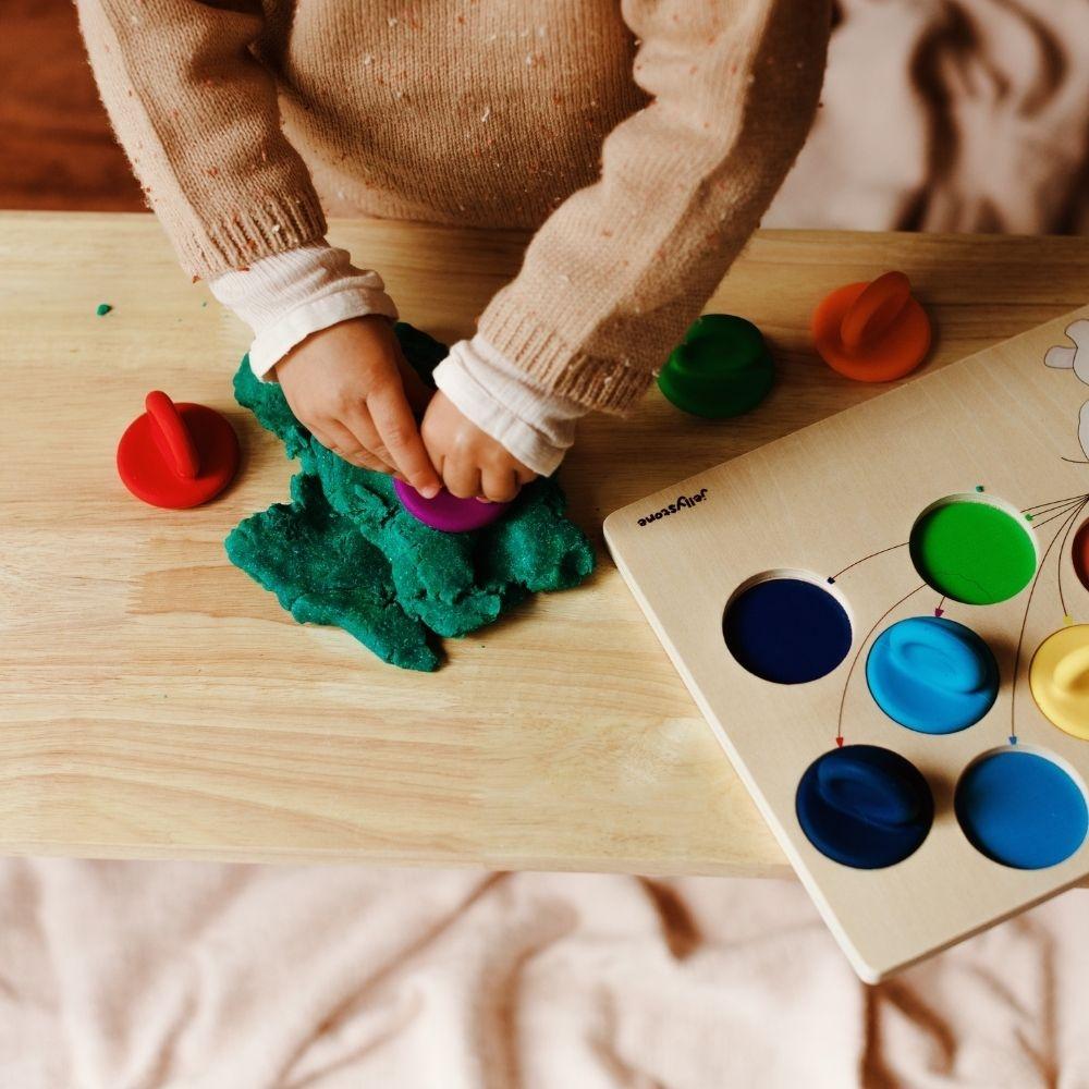 Mãos de criança a usar uma tampa de silicone colorida do conjunto Jellystone para carimbar plasticina verde, demonstrando a função de carimbo do brinquedo.
