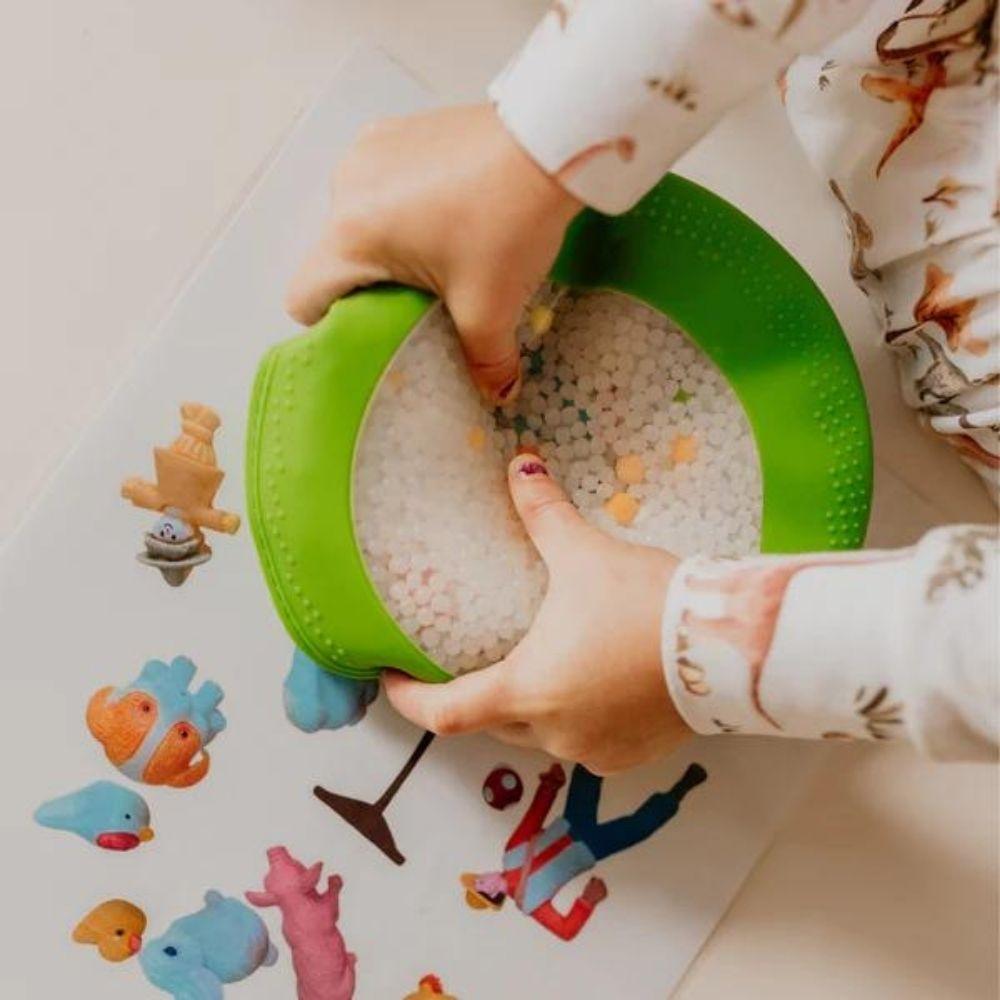 Criança a apertar a Jellystone Peekaboo Bag verde com contas e figuras visíveis.
