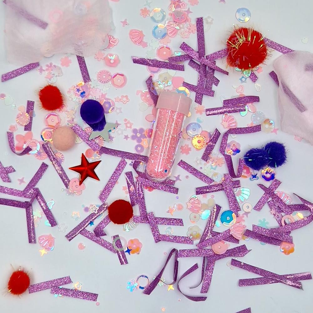 Detalhe dos elementos da recarga temática "Centelha" da Jellystone: glitter rosa, pompons coloridos, estrelas e fitas brilhantes.