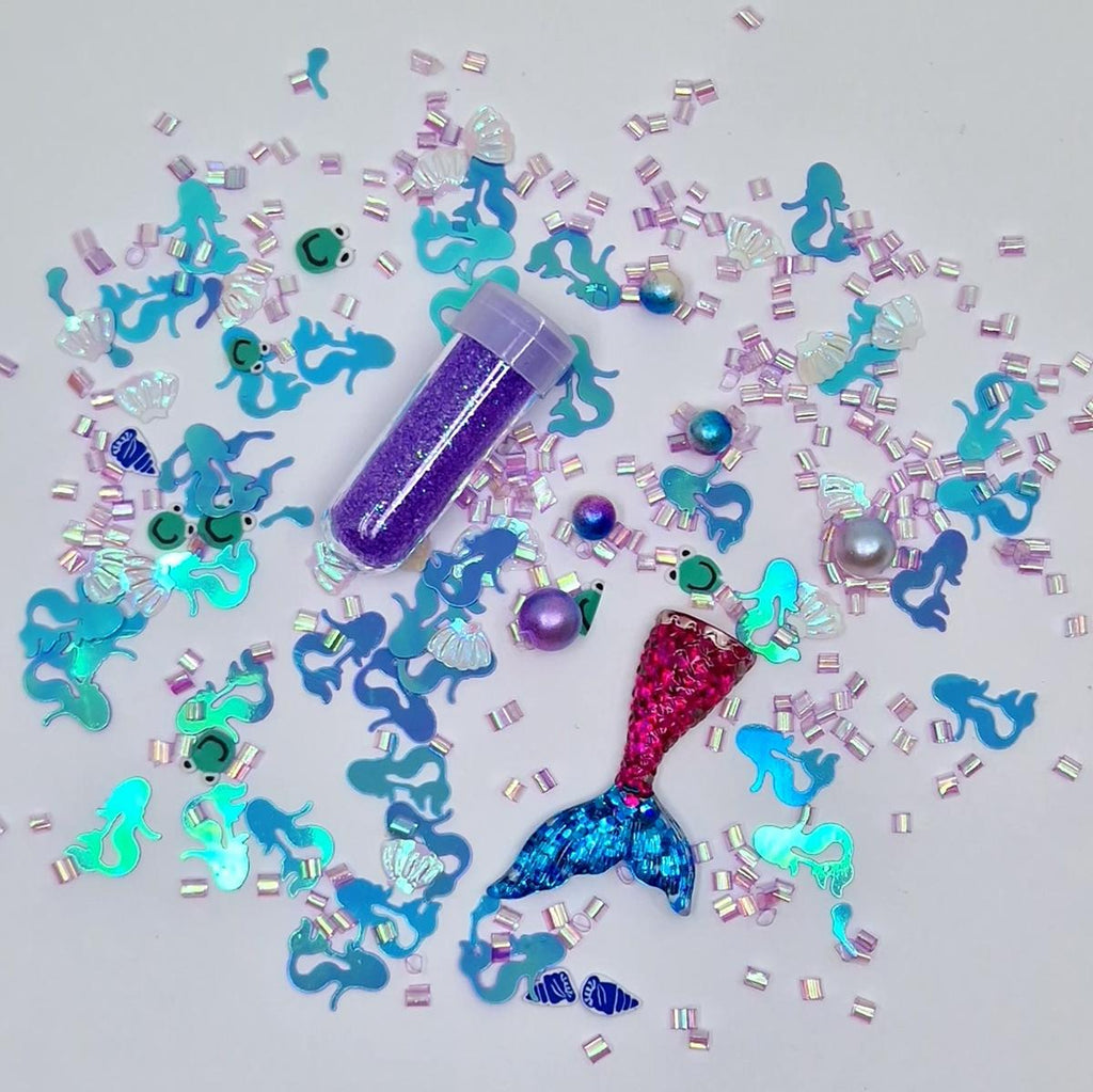 Detalhe dos elementos da recarga temática "Sereia" da Jellystone: glitter roxo, figuras de sereias, conchas e pérolas iridescentes.