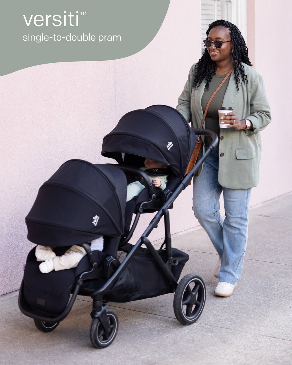 Detalhe do carrinho duplo Joie Versiti Signature preto com dois assentos, um bebé visível, e texto a indicar "single-to-double pram".
