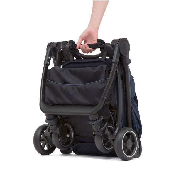 Mão a segurar a pega de transporte do carrinho Joie Pact dobrado, mostrando o fecho compacto e a capacidade de ficar de pé sozinho.