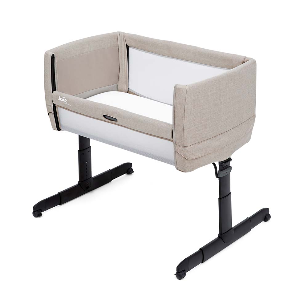 Berço de co-sleeping Joie Roomie Go montado ao lado de uma cama de adulto, mostrando o painel lateral rebatido para acesso fácil ao bebé.