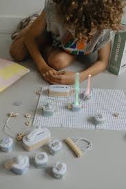 Criança com cabelo encaracolado a brincar no chão com os componentes do kit elétrico KIDYELEC, montando um circuito com luzes.
