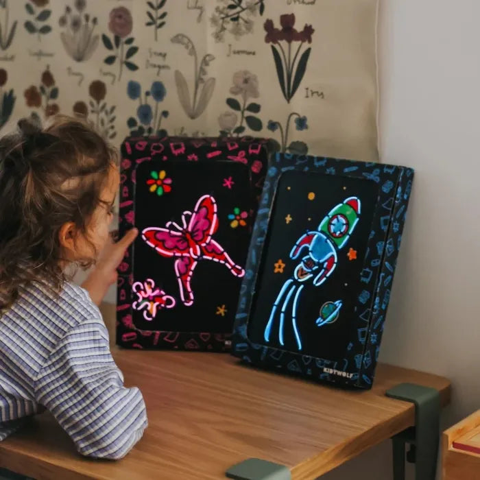 Duas placas de arte neon da KidyWolf, uma borboleta rosa e um foguetão azul, expostas numa secretária.