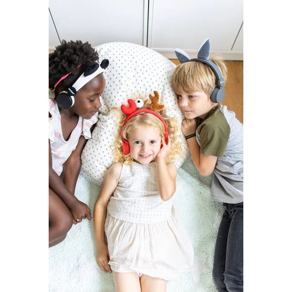 Três crianças deitadas a usar auscultadores KidyWolf com diferentes designs de animais, incluindo o de caranguejo, a partilhar um momento de audição.