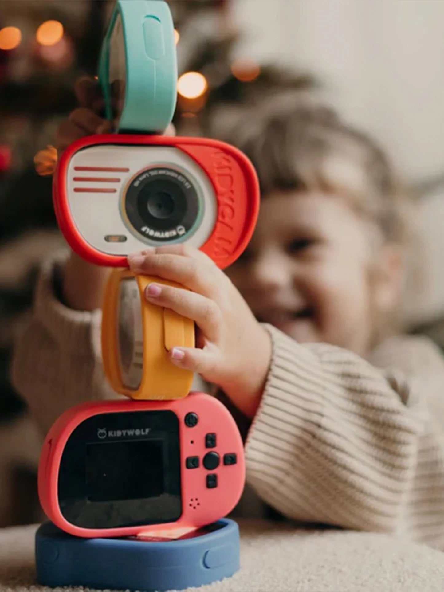 Criança a empilhar três máquinas fotográficas Kidywolf de cores diferentes (azul, laranja, rosa), demonstrando a modularidade e o uso divertido.