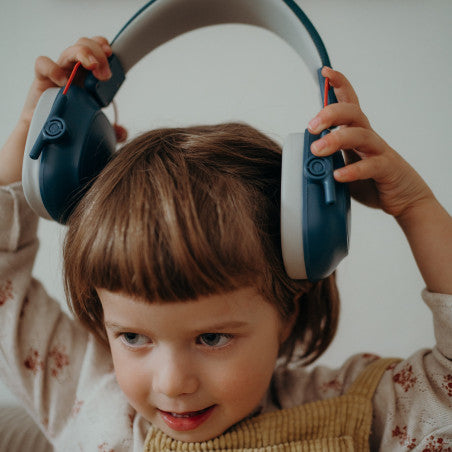 Criança pequena a colocar protetores auditivos azuis escuros KidyWolf na cabeça, demonstrando o ajuste ergonómico e conforto.