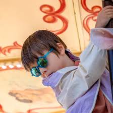 Criança com cabelo escuro a usar os óculos de sol Kietla RoZZ de armação azul-petróleo, num carrossel, protegendo os olhos.