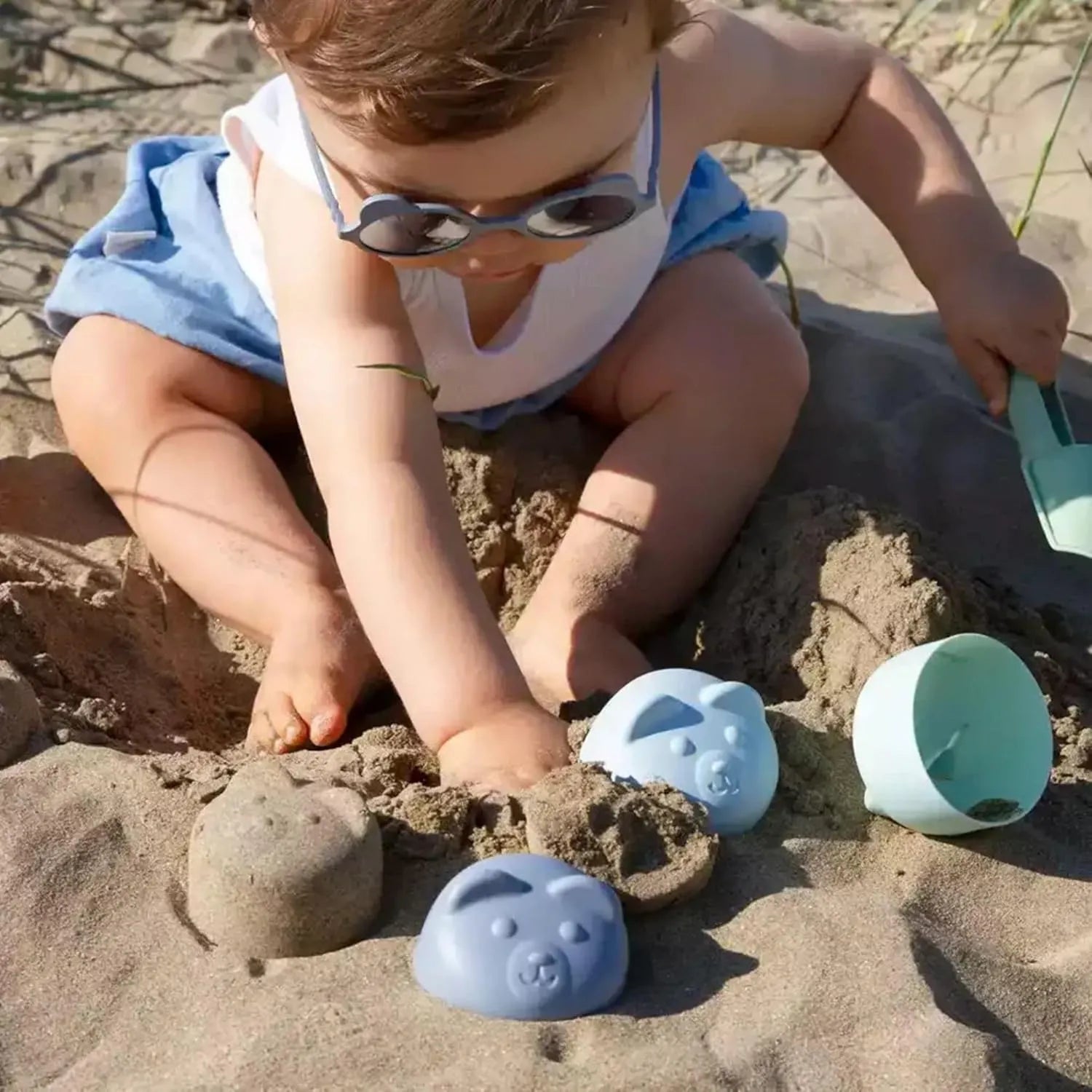 Bebé brincando na praia usando os óculos de sol Kietla Urso Almond Green, destacando a proteção solar e o conforto.