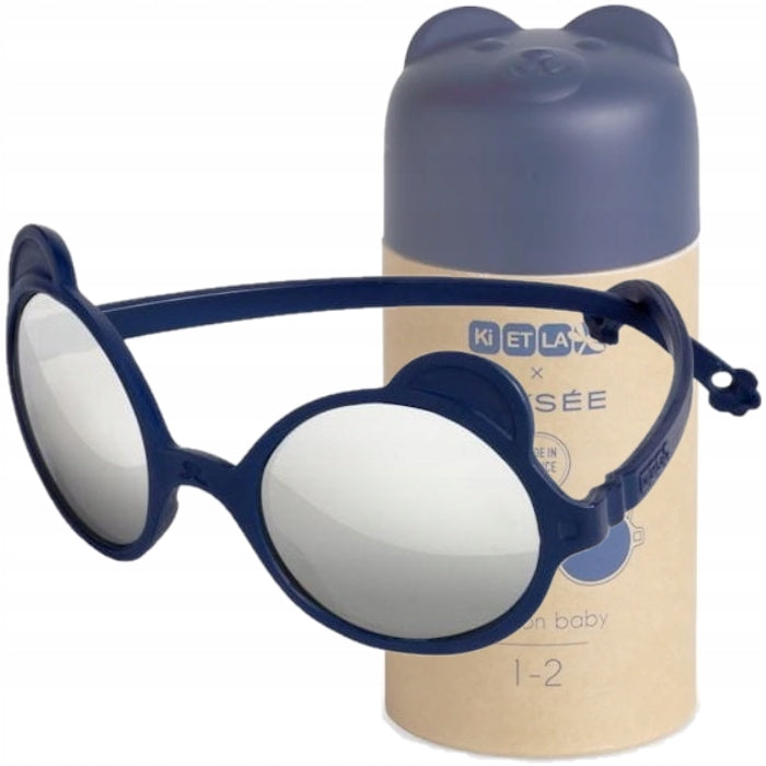 Óculos de sol Kietla Urso Bleu azuis com detalhes de orelhas de urso, em primeiro plano junto ao seu estojo cilíndrico de cartão.