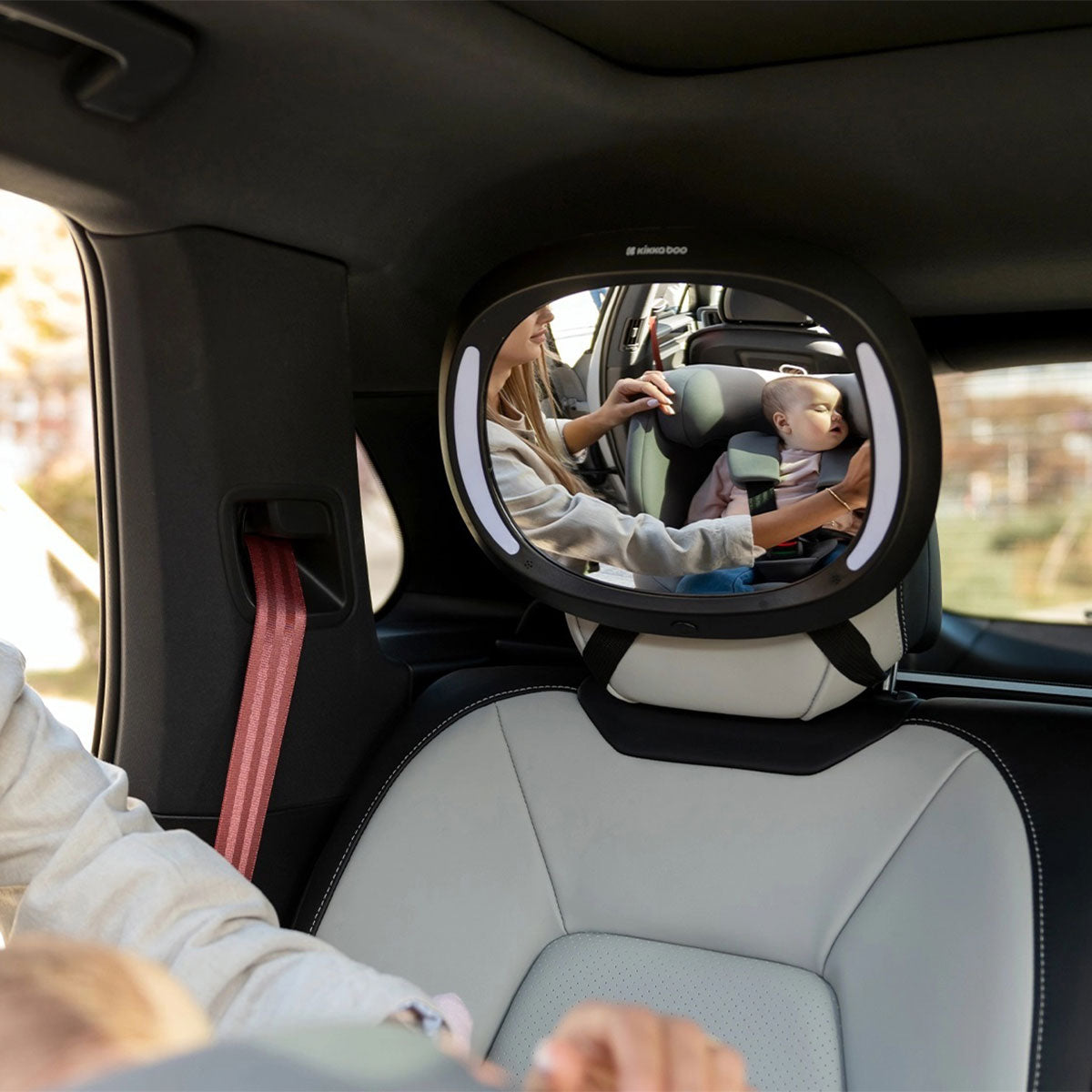 Mãe a ajustar o espelho auto Kikkaboo com LED para ver o bebé na cadeira auto virada para trás.