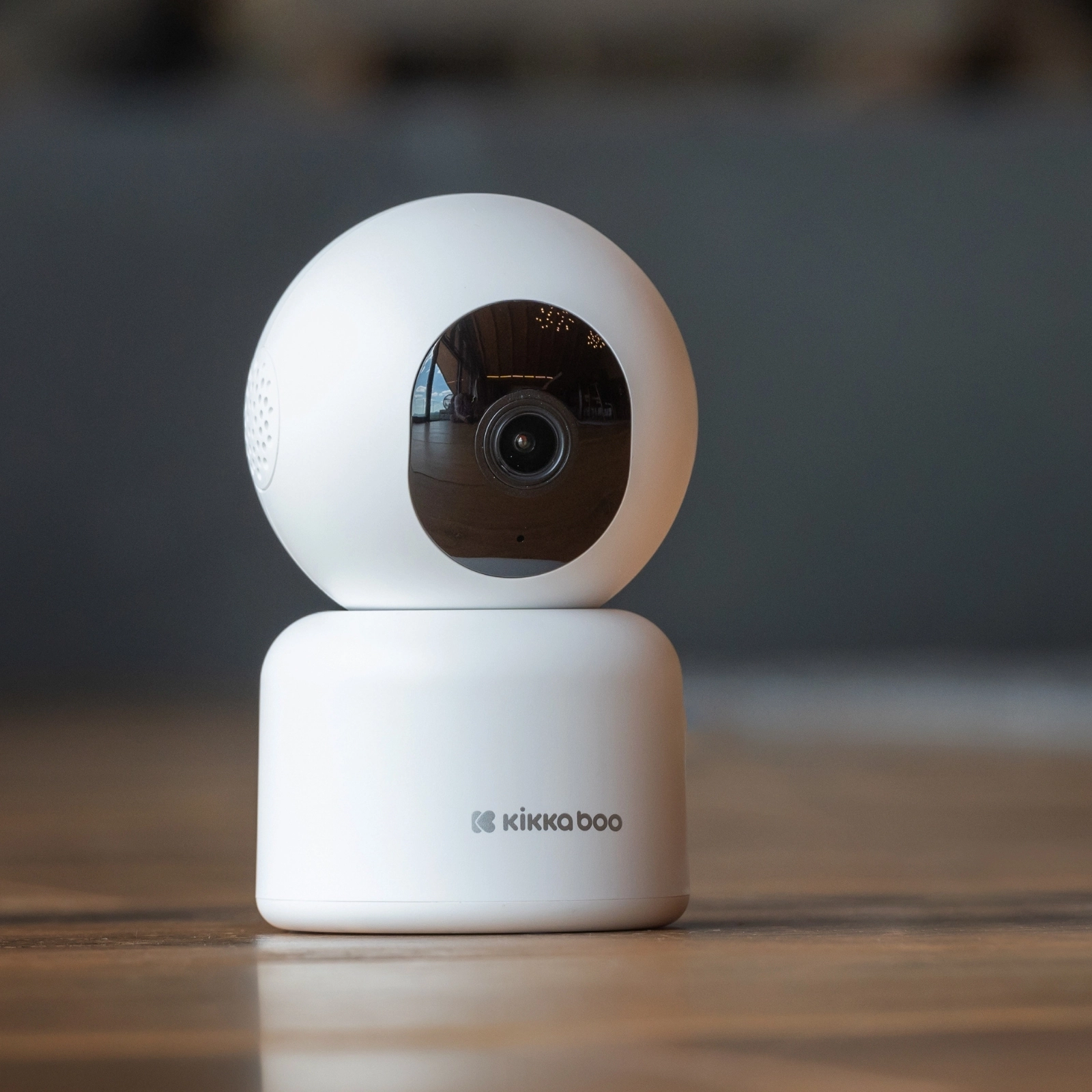 Câmara KikkaBoo Wi-Fi Arlo branca numa superfície de madeira, num ambiente doméstico, mostrando a sua utilização prática.