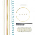 Componentes do kit de macramé: aro de madeira, rolo de fio branco, fitas coloridas, fita com pompons azuis, contas de madeira, um pente preto e um giz branco.