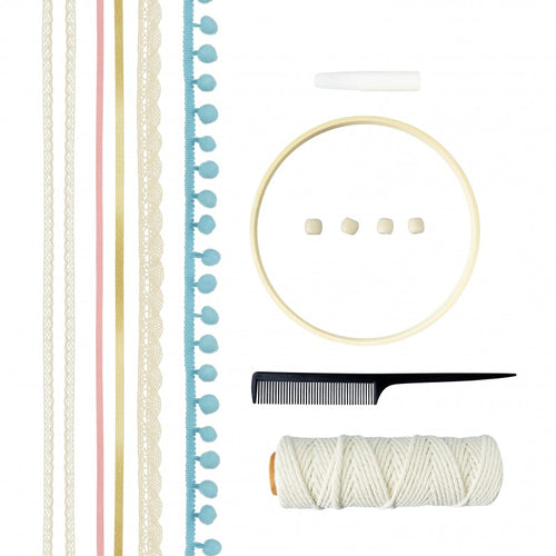 Componentes do kit de macramé: aro de madeira, rolo de fio branco, fitas coloridas, fita com pompons azuis, contas de madeira, um pente preto e um giz branco.