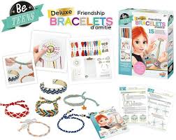 Vista geral do conteúdo do kit 'Deluxe Friendship Bracelets', exibindo os fios de algodão, ferramentas de tecelagem, manuais e exemplos de pulseiras finalizadas em vários padrões.