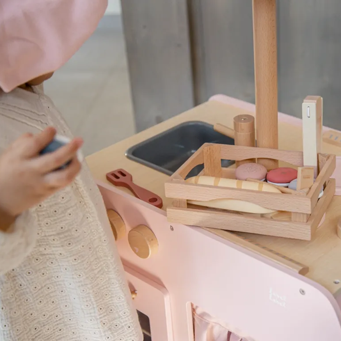 Criança a brincar com o conjunto Label Label Pastelaria numa cozinha de brincar cor-de-rosa.
