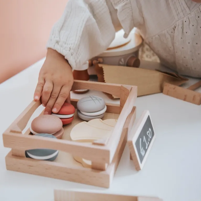 Mãos de criança a pegar num macaron de madeira do conjunto Label Label Pastelaria numa caixa de madeira.