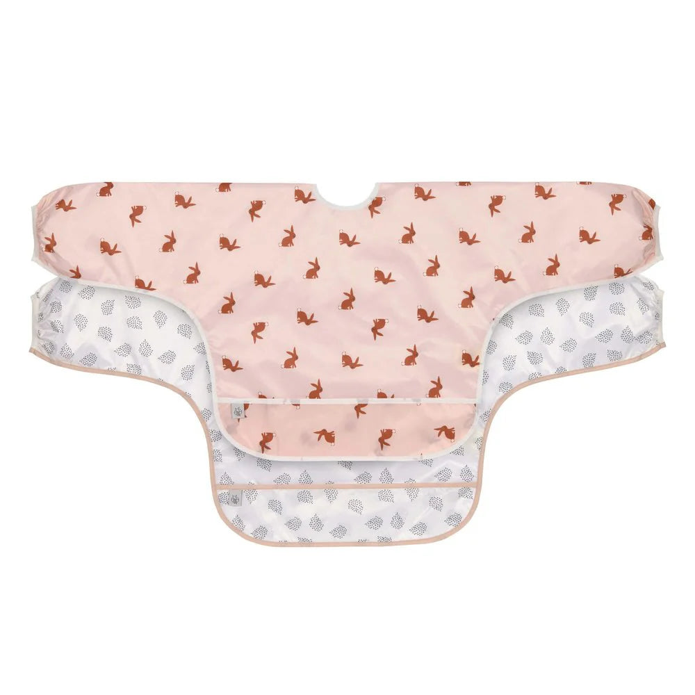 Pack de 2 babetes Lassig com mangas, um rosa coelho e outro branco padrão, ideais para 6-24 meses.