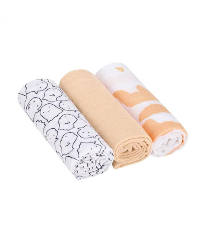 Três musselinas Lassig enroladas: uma com padrão fantasma preto/branco, uma lisa cor pêssego e uma com padrão abstrato laranja/branco.